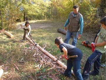 Vom Baum zum Zaun: Kinder beim Entrinden von Lärchenrundholzstämmen